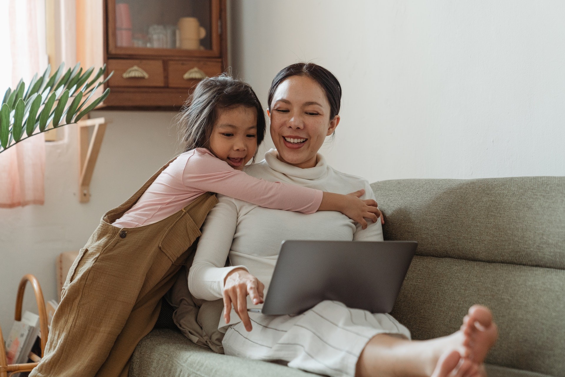 Mother and child on a computer while sitting on a couch.
