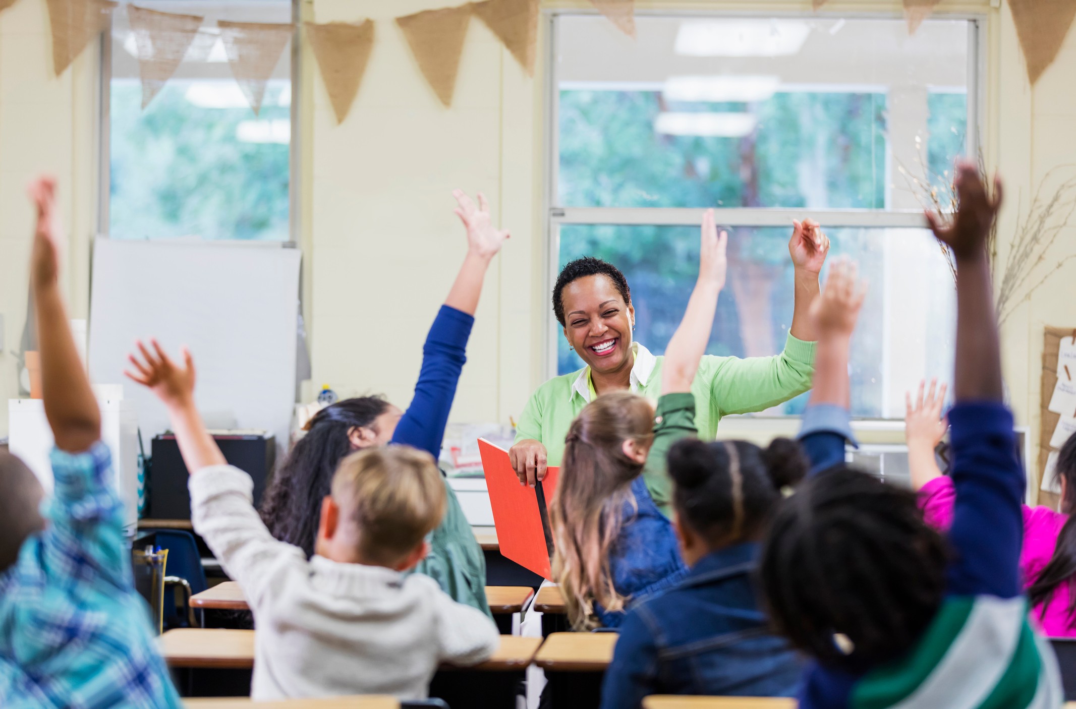 Teacher sitting in front of her class of students with their arms raised