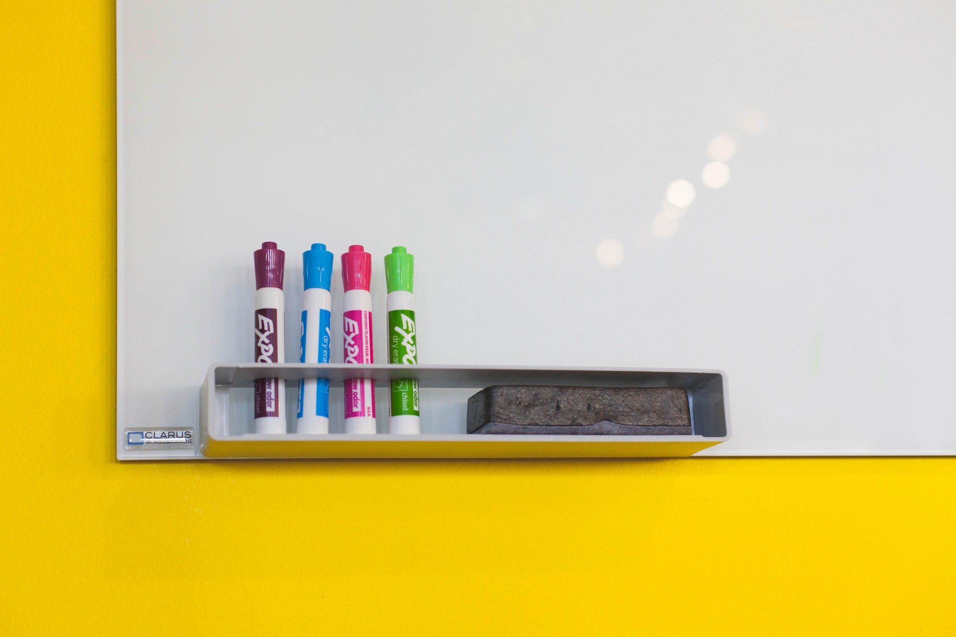 Whiteboard on a yellow wall with markers and an eraser.