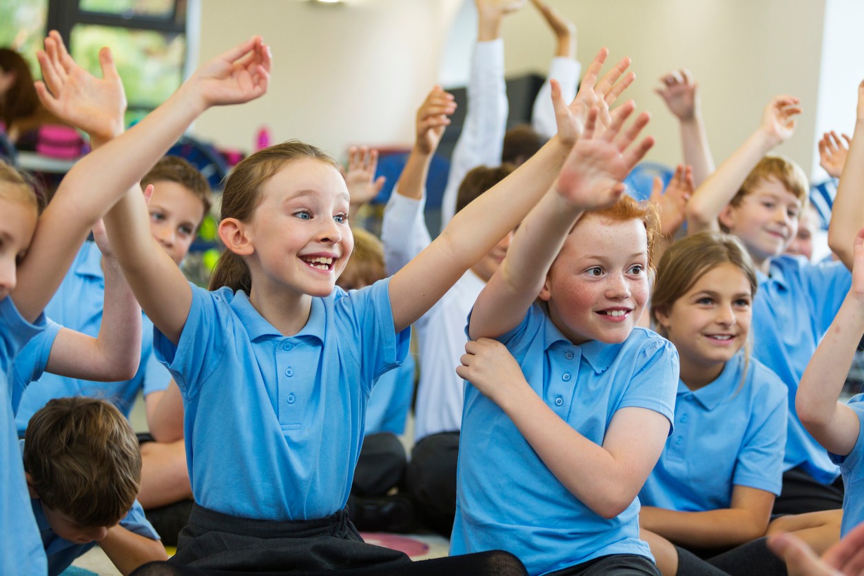 Excited students raise their hands to answer ice breaker questions for kids in their classroom