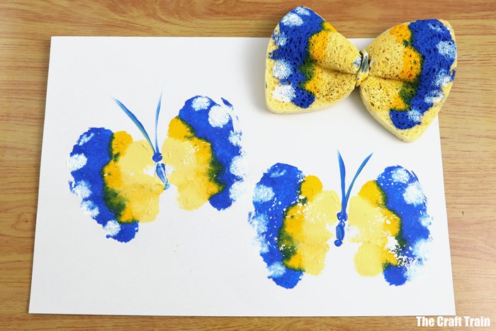 Blue and yellow butterfly painting with paint-covered kitchen sponge above it.