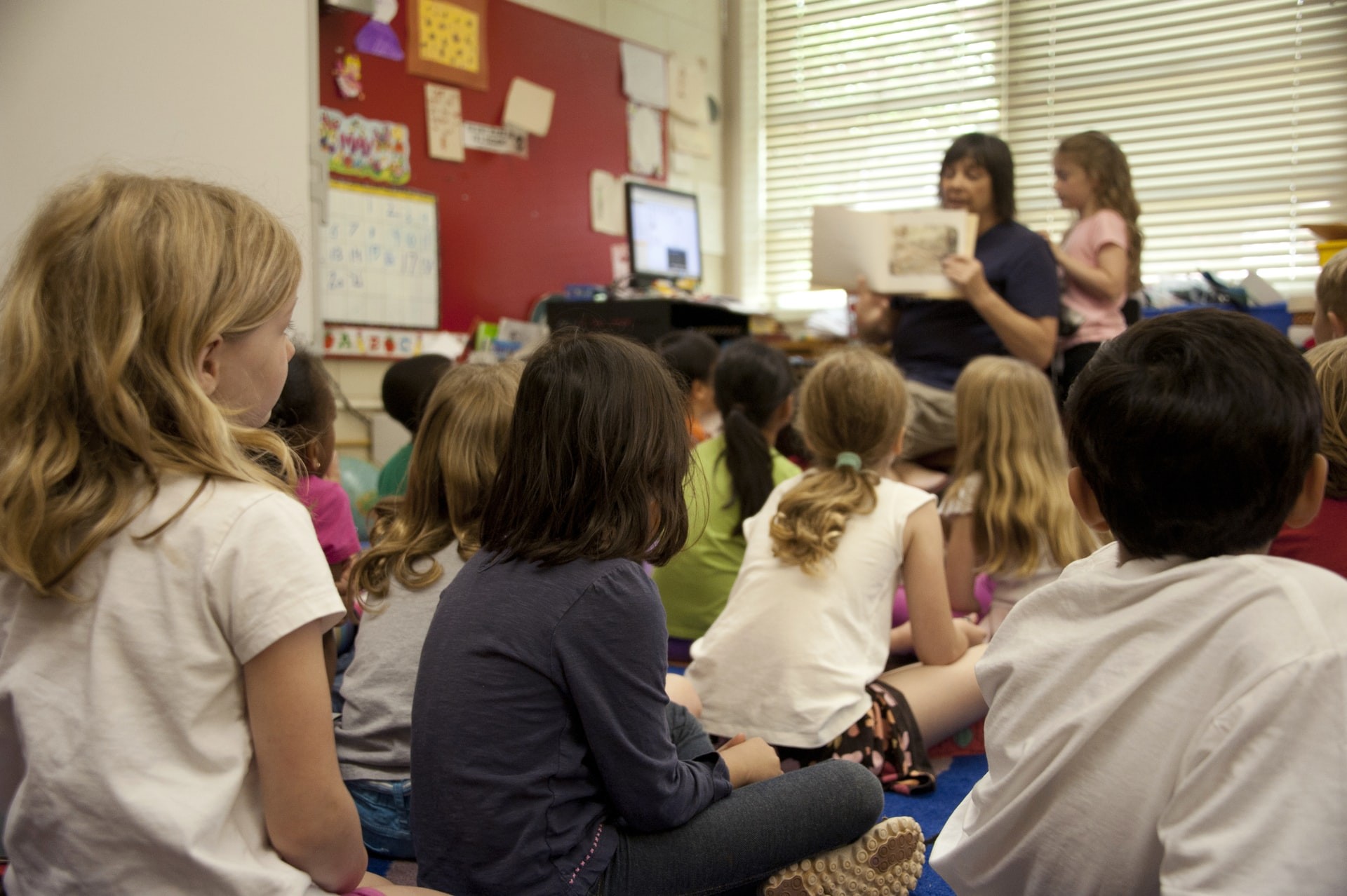 A teacher reading a picture book to a group of students sitting on floor mats as they work on improving reading comprehension skills. 