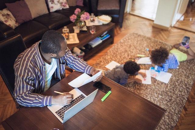 Father of two looks over at his kid doing homework on the carpet