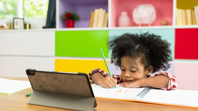 Girl writing in front of tablet.