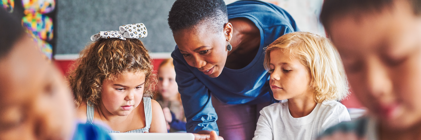 A teacher bends down to talk to two students in a classroom during teacher appreciation week.
