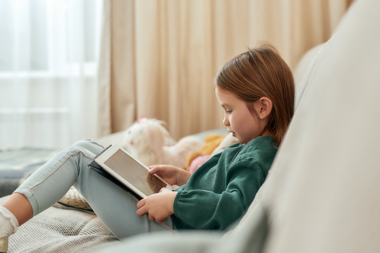Second-grade child sitting on the couch, using a tablet to learn.