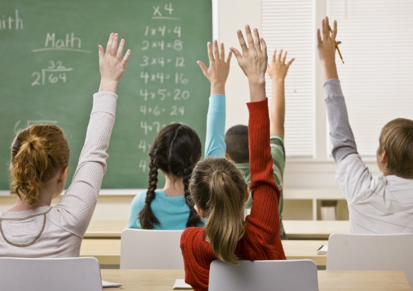 A classroom of young students with their hands raised to answer.