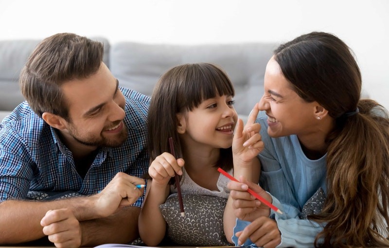 Child smiles and plays with her parents as they write in a journal together.