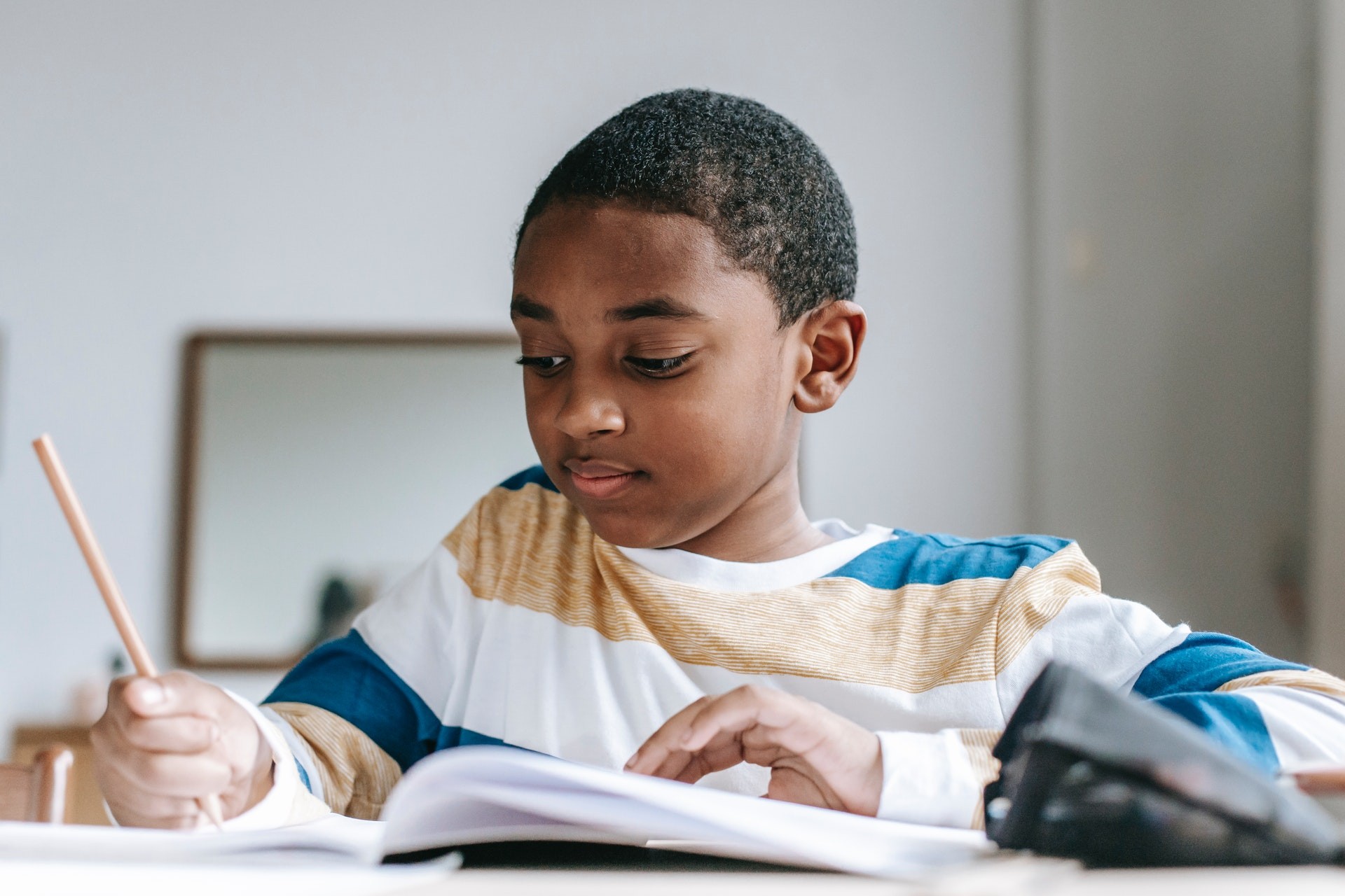 Young boy sits at a desk with a notebook and pencil writing a story.
