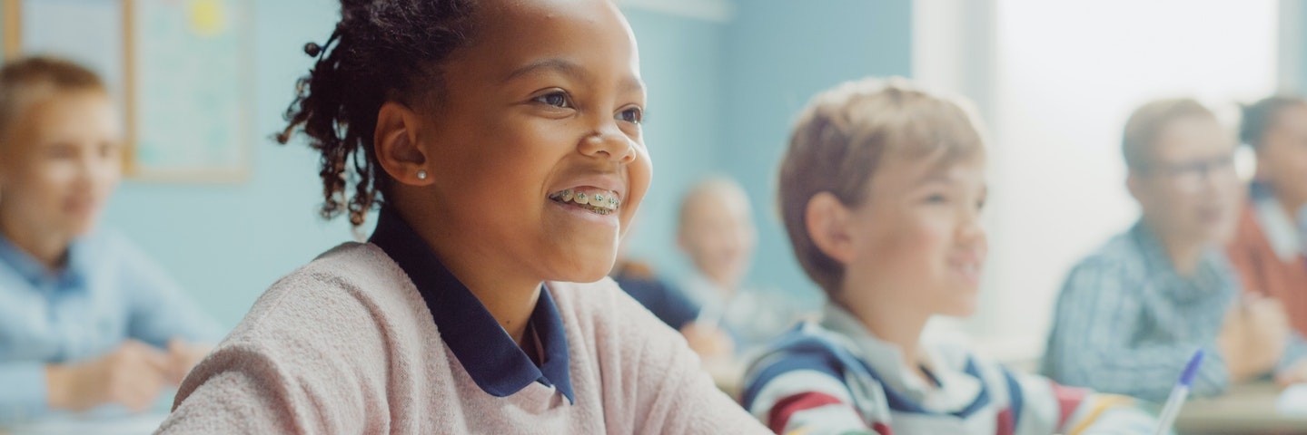Young girl sits in a classroom smiling as she learns how to do long division.
