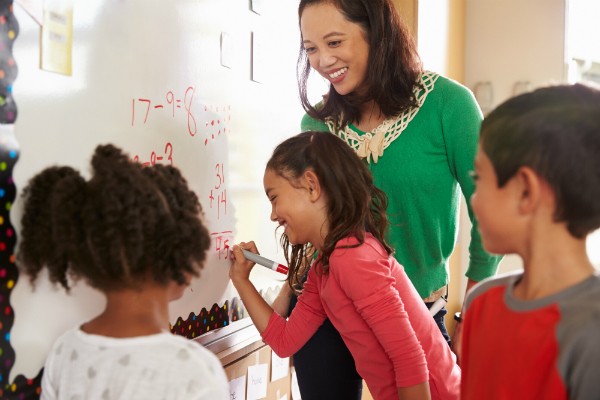 A teacher is teaching three students with a whiteboard happily.