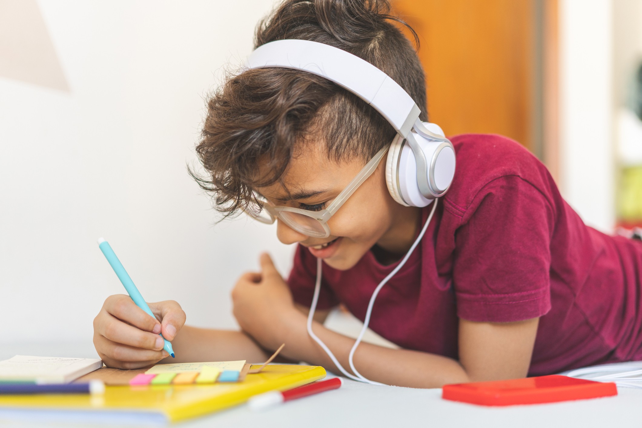 Child listening to headphones and smiling while writing notes. 