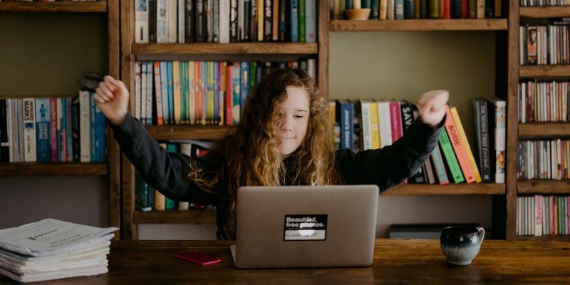 Student using laptop and raising arms in excitement.