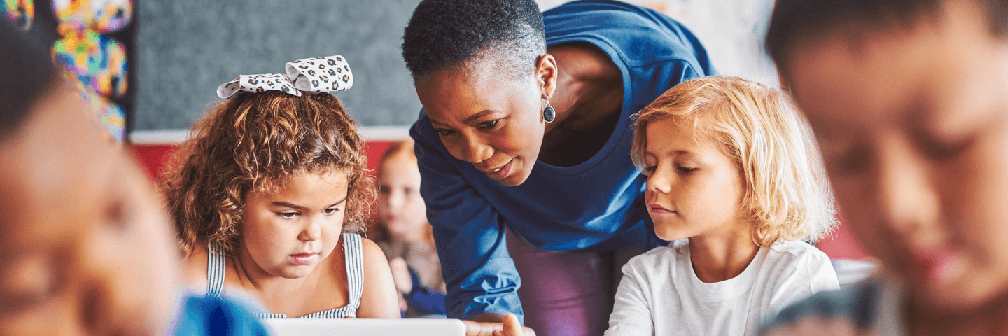 A teacher bends down to talk to two students in a classroom during teacher appreciation week.