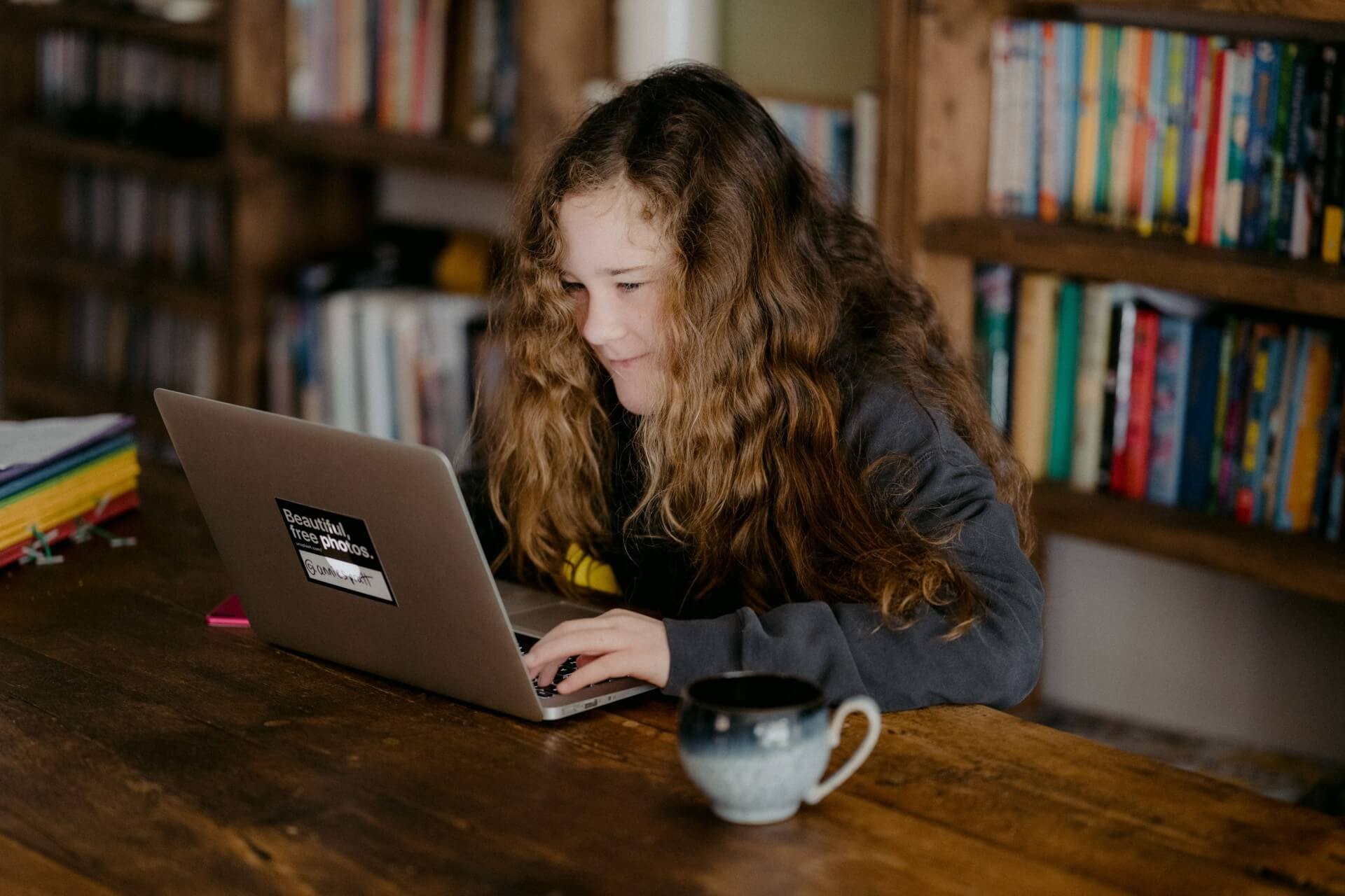 Girl at a table smiles while on a laptop.