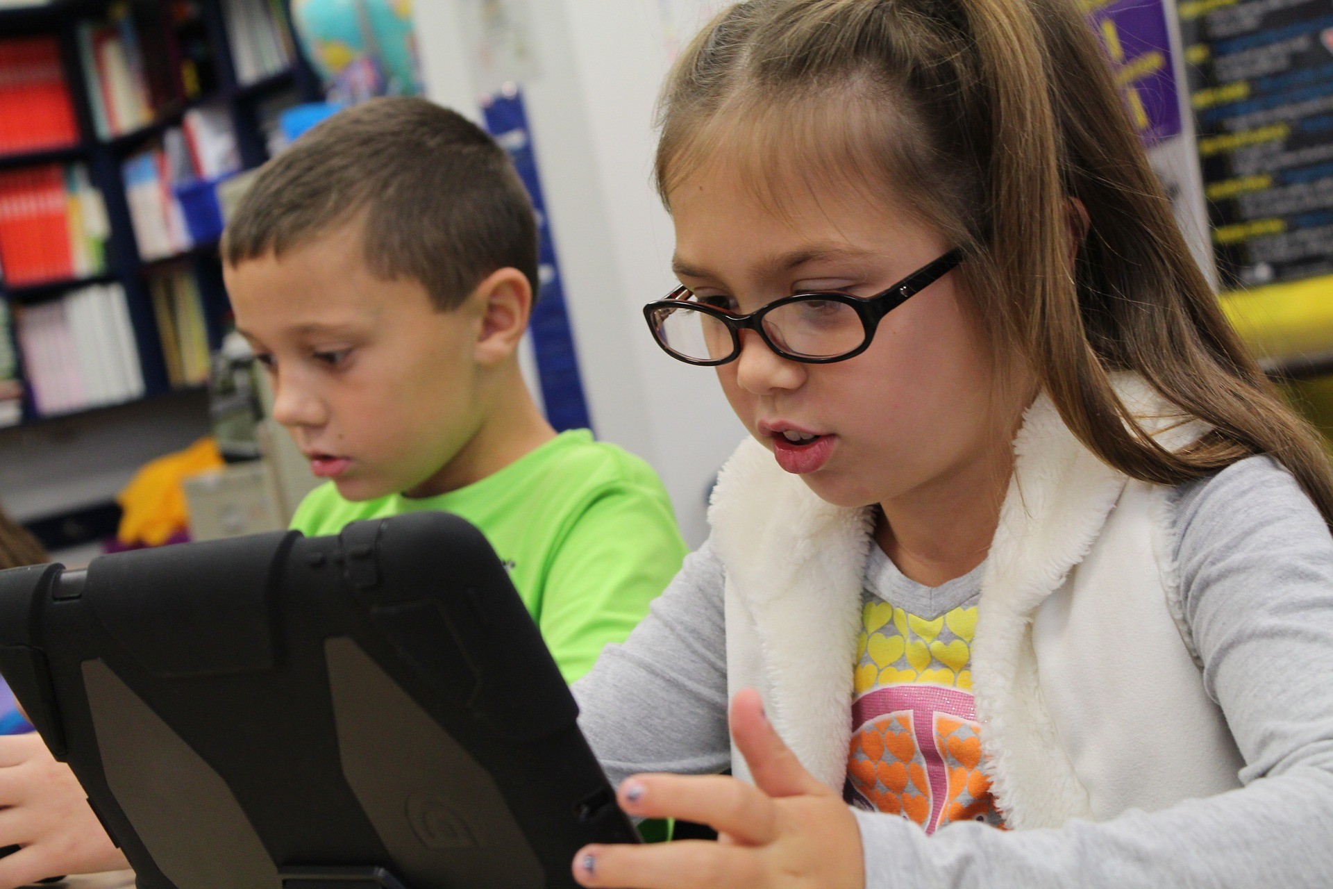 Two children work on tablets in a classroom.