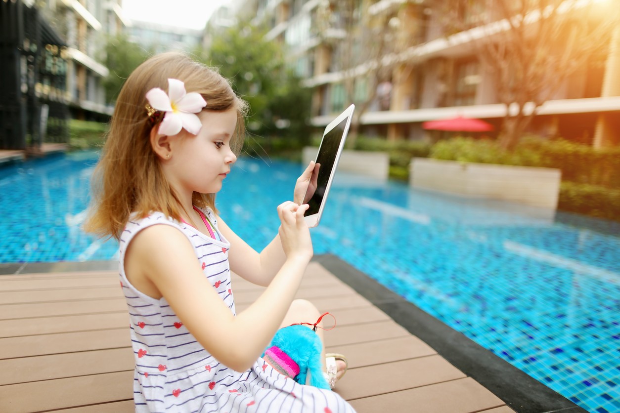 Child sitting by a pool on a tablet device. 