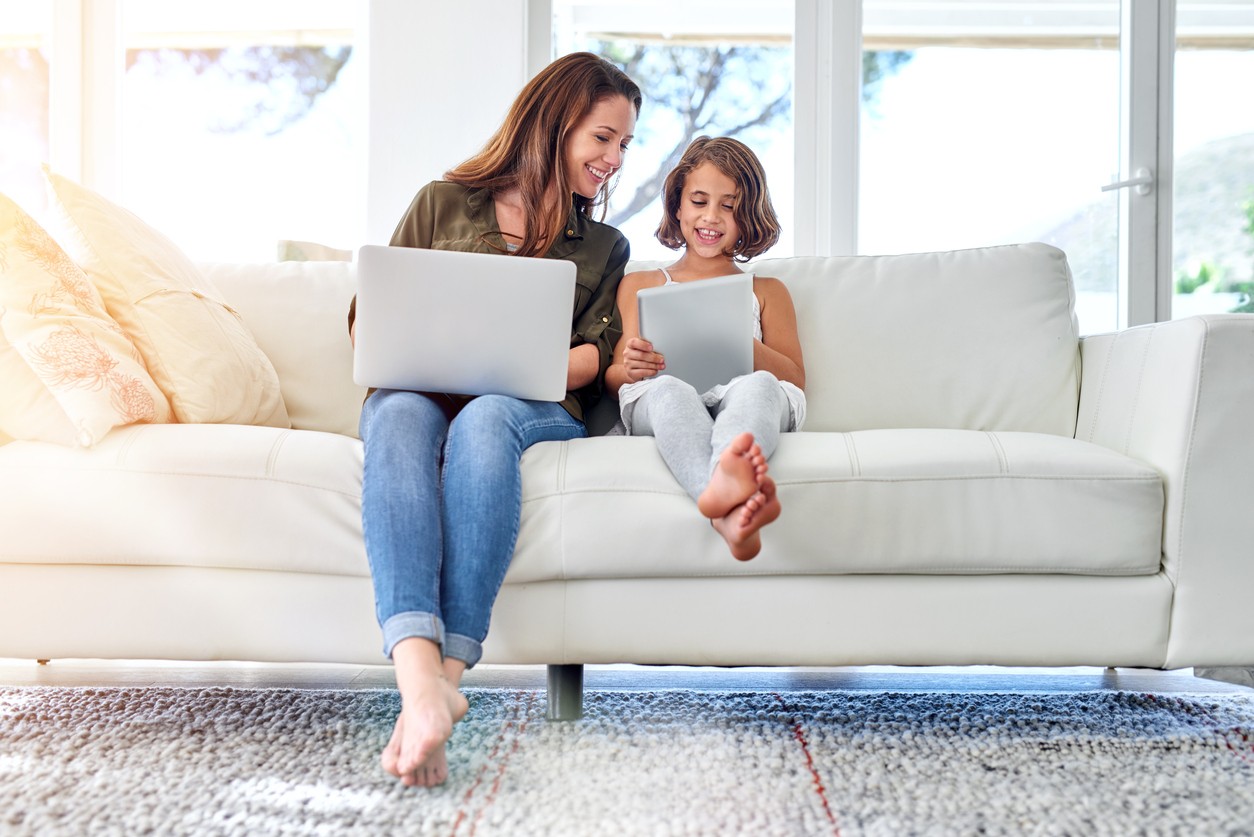 mother and daughter sitting on a couch together on their laptops