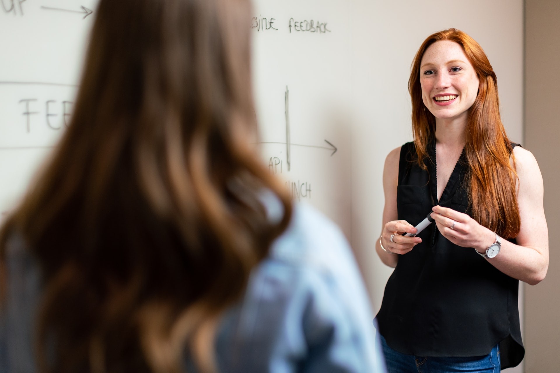 A teacher talks to a student while standing in front of a whiteboard.