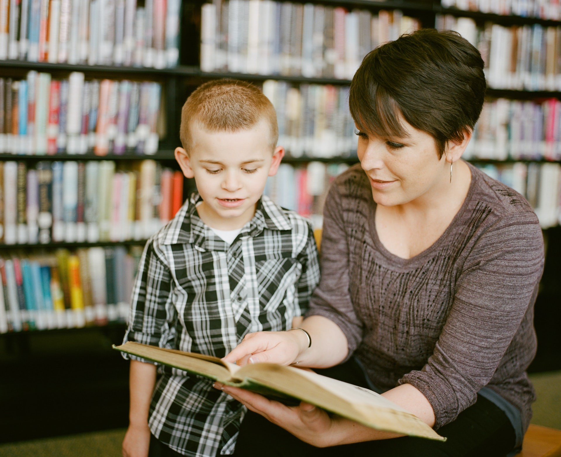 A teacher and a student read a book together in a library while working on reading strategies.