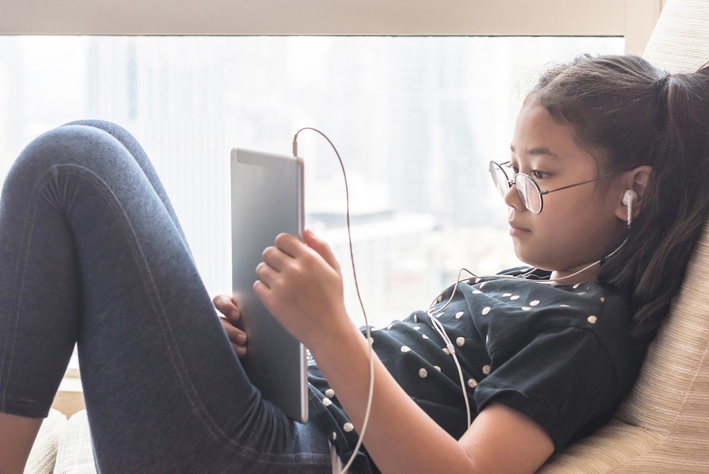 Child relaxing on the couch while using an online reading program on her tablet device.