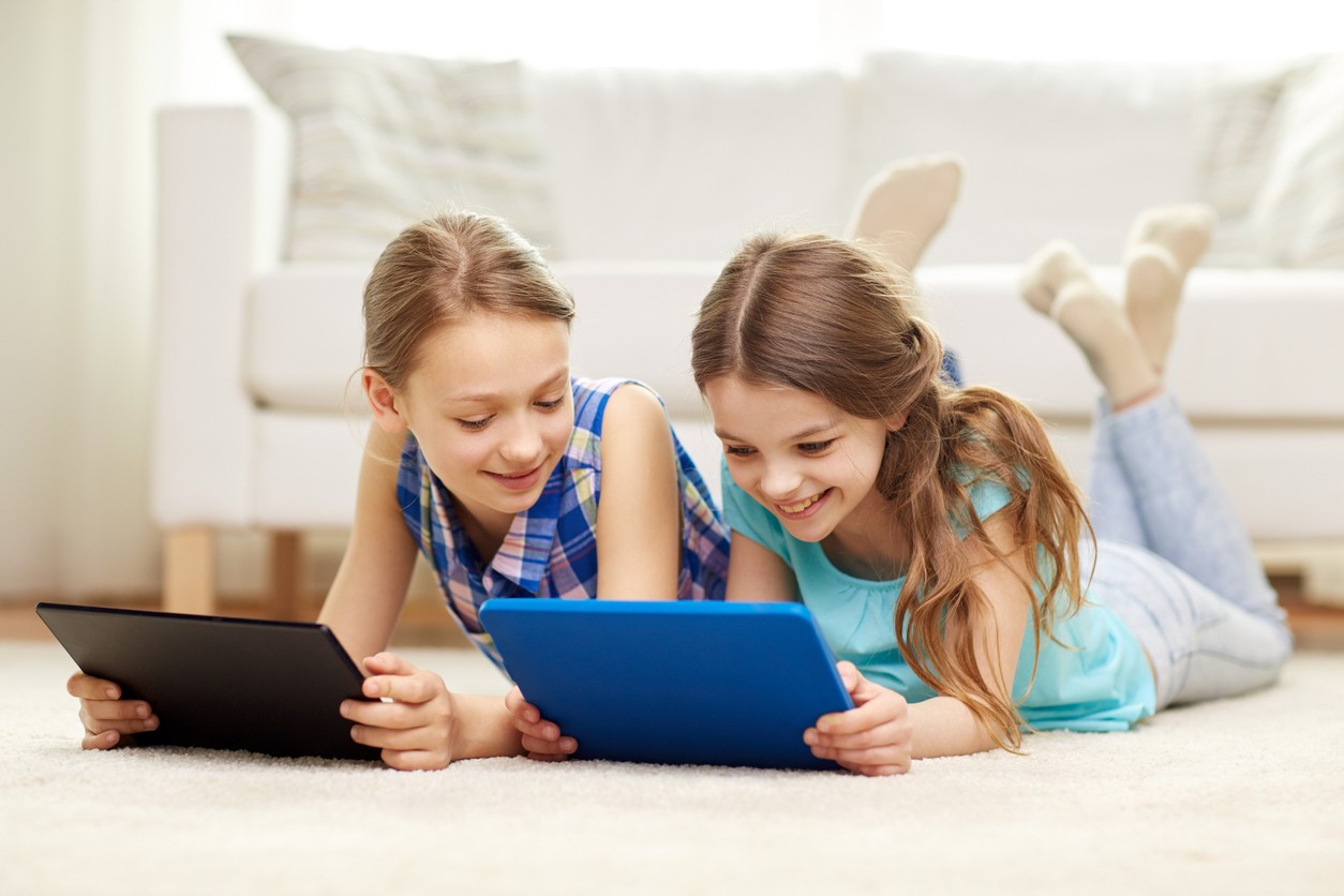 Two girls smiling while playing on tablets.