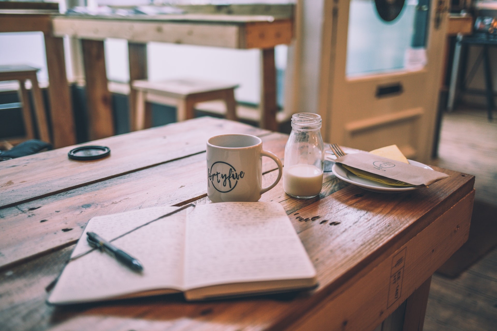 Journal, coffee mug and plate on a cafe table as part of a teacher self-care routine.