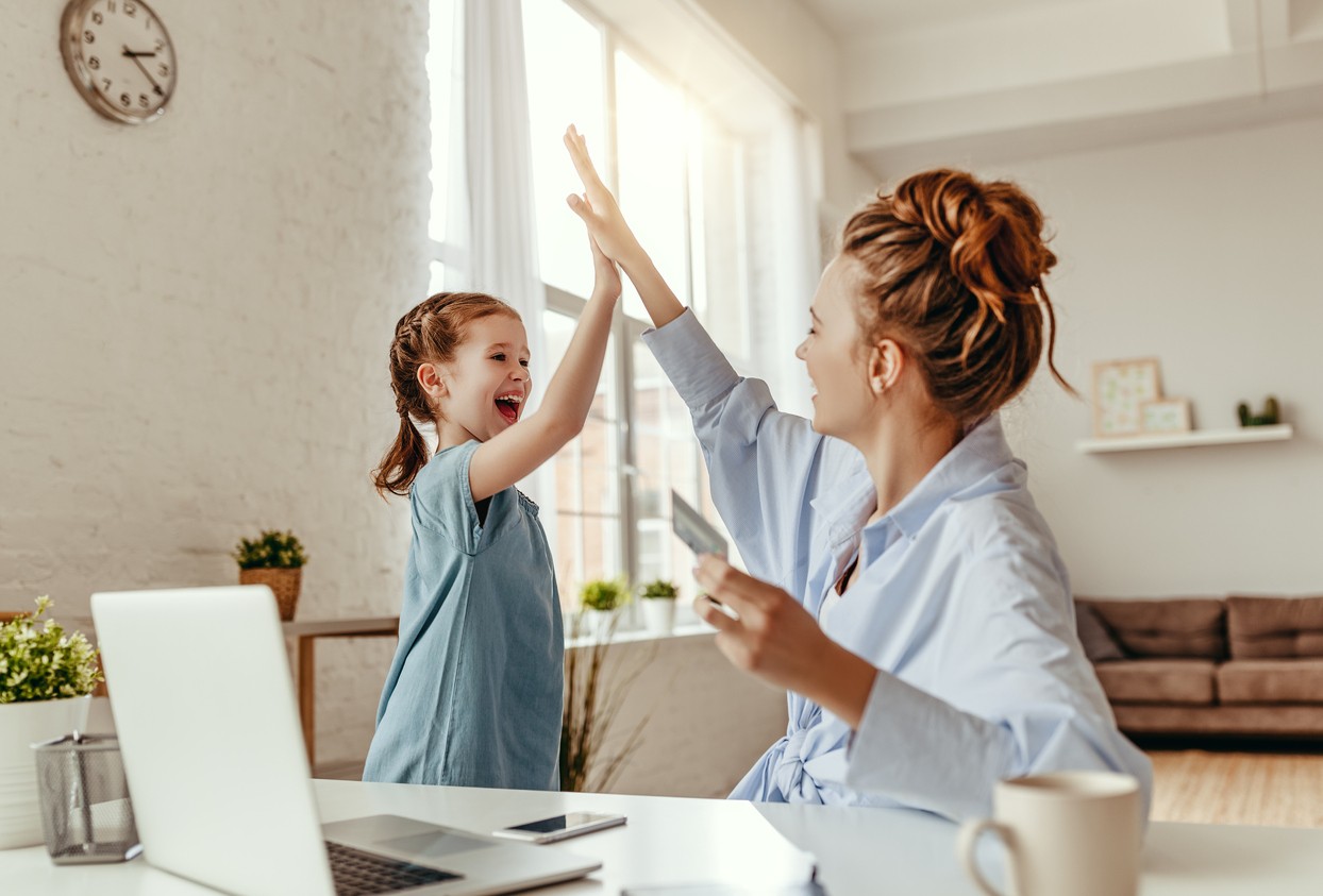 Mother and daughter high-fiving in front of the computer after completing a family financial goal.
