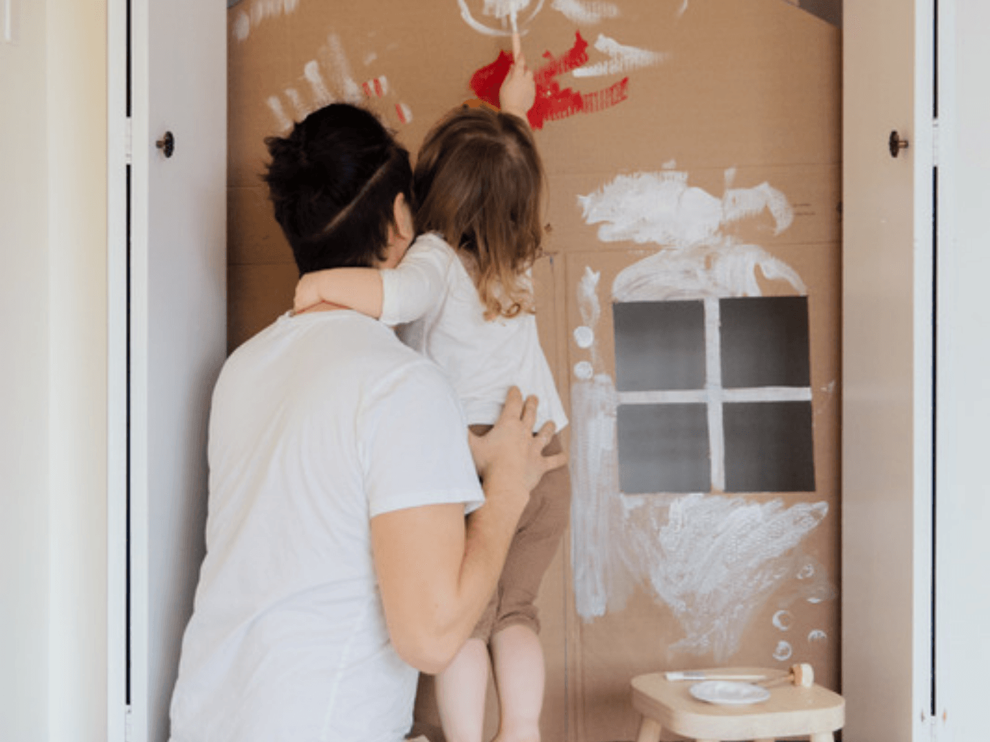 Father and child painting a cardboard house together for their family home project goal.