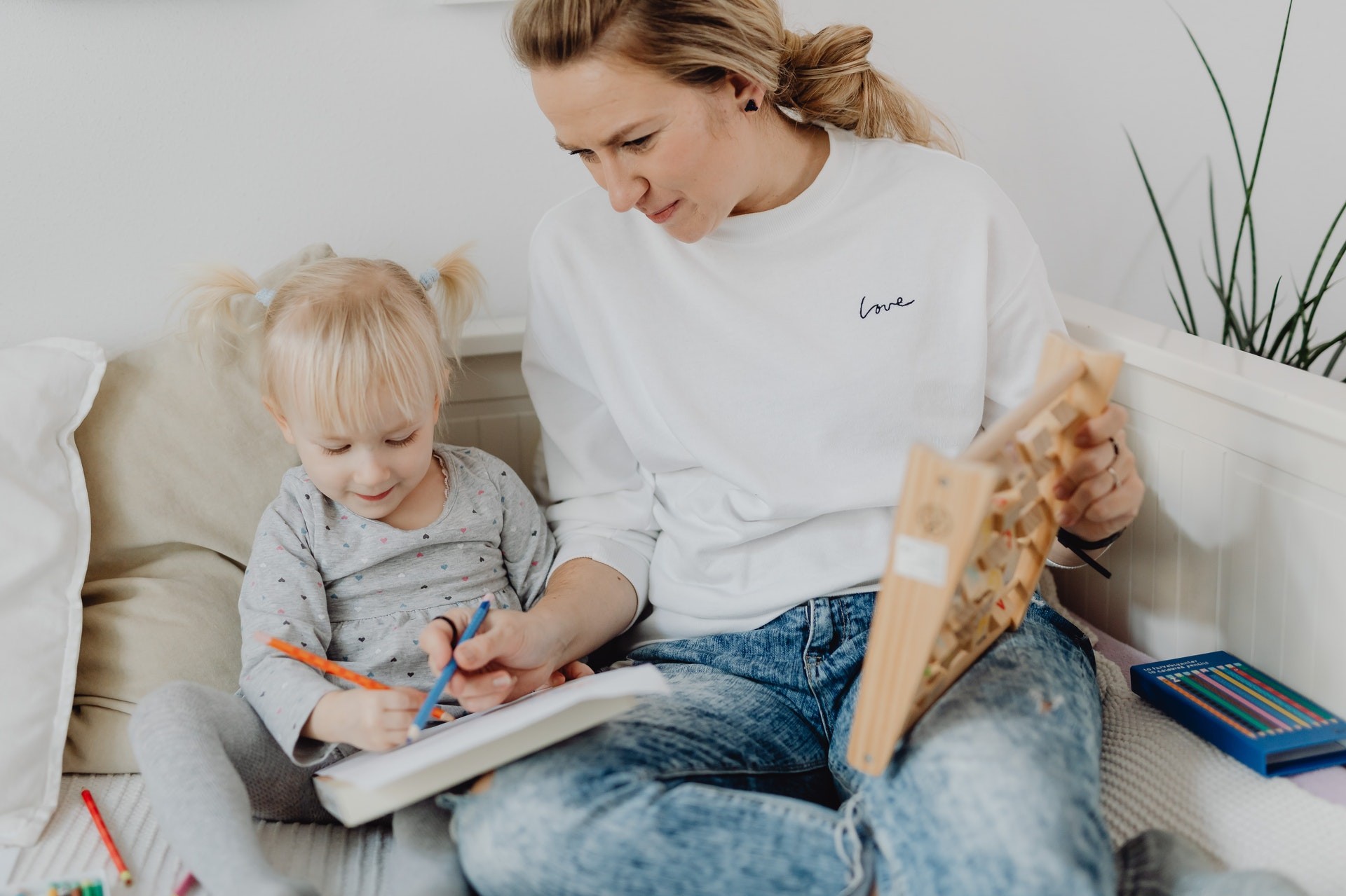 A mother and child sit on the couch and do reading activities together.