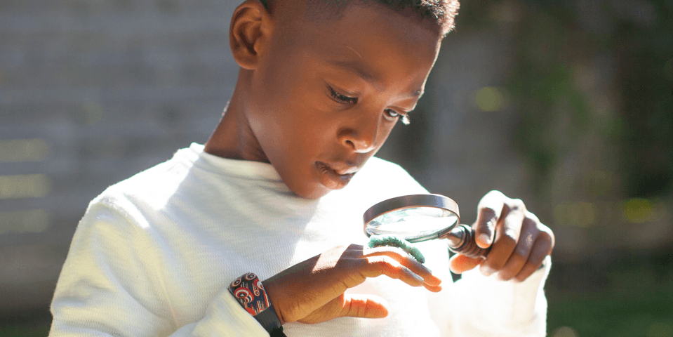 Child using a magnifying glass to look at a caterpillar on their hand.