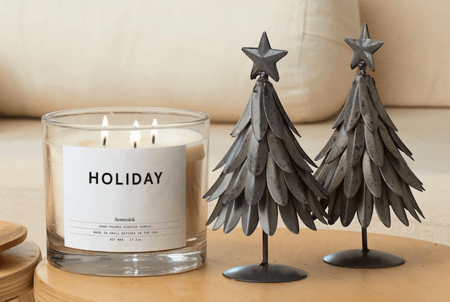 3-wick candle with "Holiday" written on label, sitting beside two mini christmas tree models.
