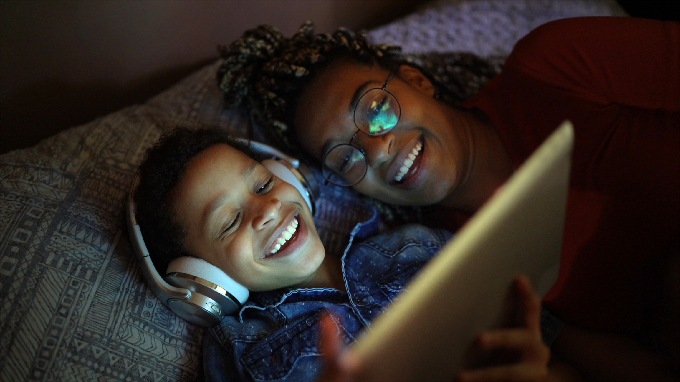 Parent and child smiling together while using a tablet device.