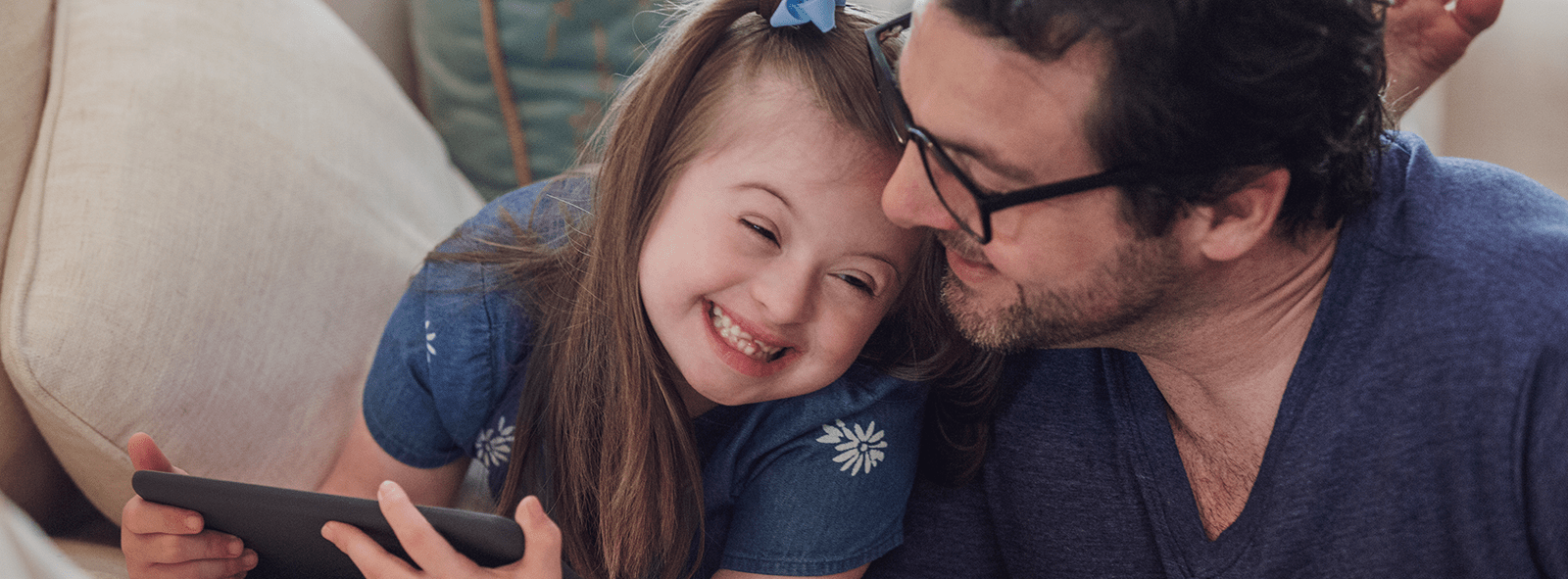 A daughter and her father laugh while playing on a tablet.