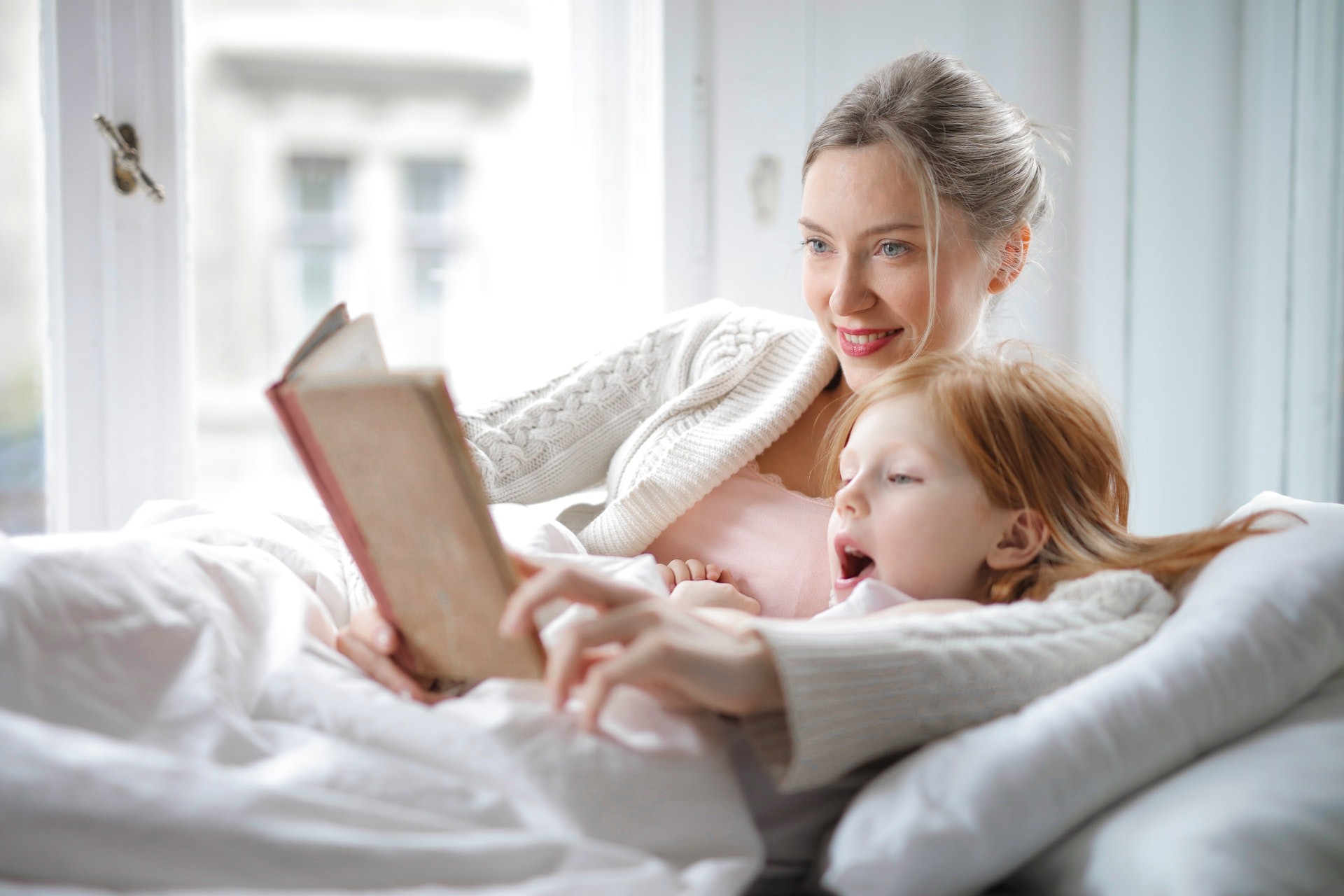 A mom and daughter lie in bed and read.