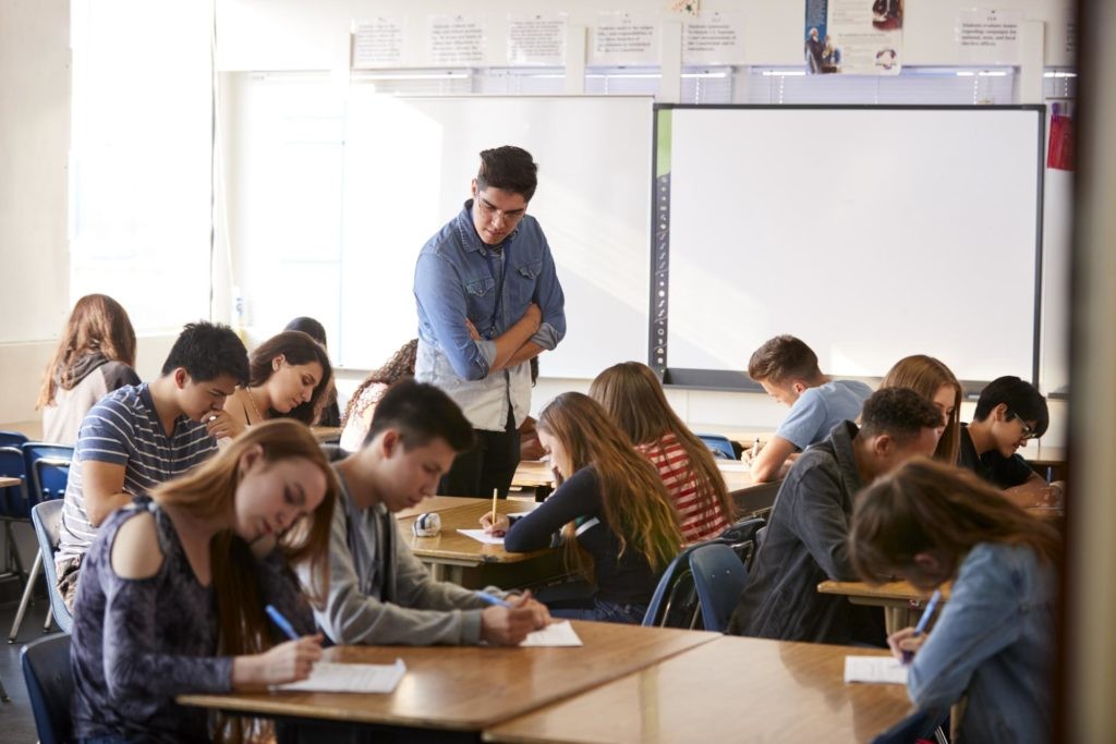 Teacher in classroom supervising students completing a test