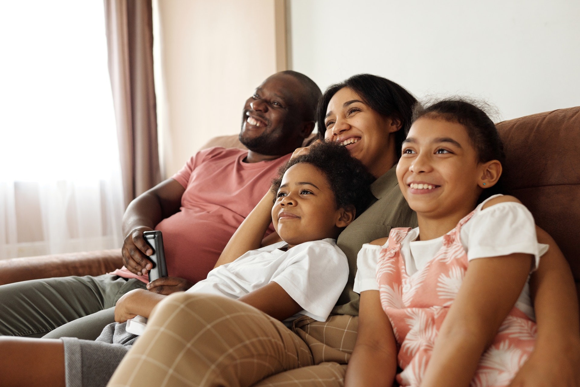 A family of four sits on a couch and smiles at a TV offscreen while they do earth day activities.