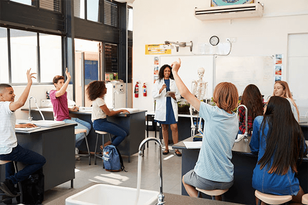 A teacher is asking questions and three student are rising their hands in a medical classroom
