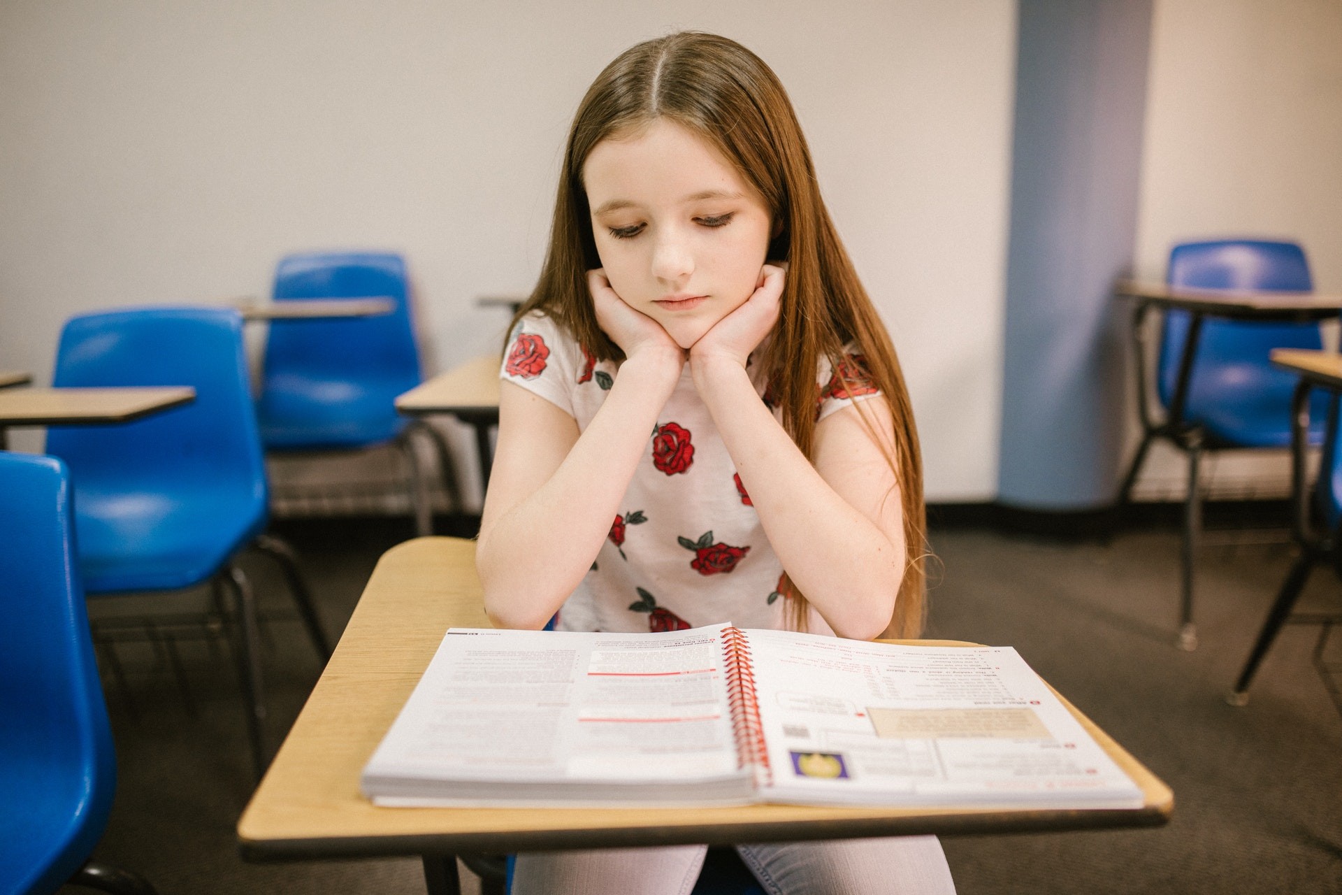 A young girl sits at a desk and looks at a reading workbook during reading activities.