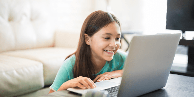Child smiling while she uses Prodigy on her computer.  