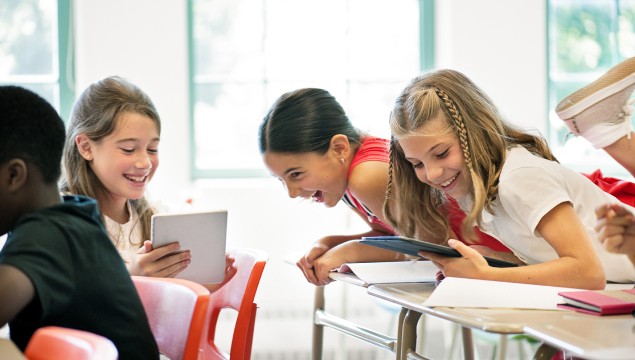 Students laughing in classroom while learning with tablet