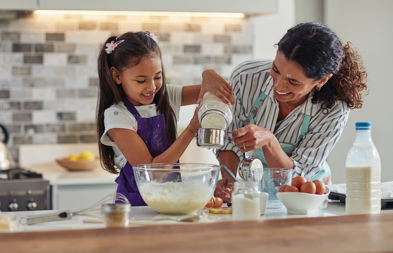 Mother and daughter baking together, measuring ingredients to help the child learn more math at home.