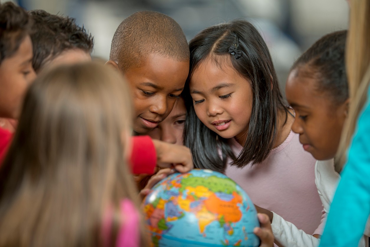 A diverse group of students gathering around a spinning globe in their classroom.