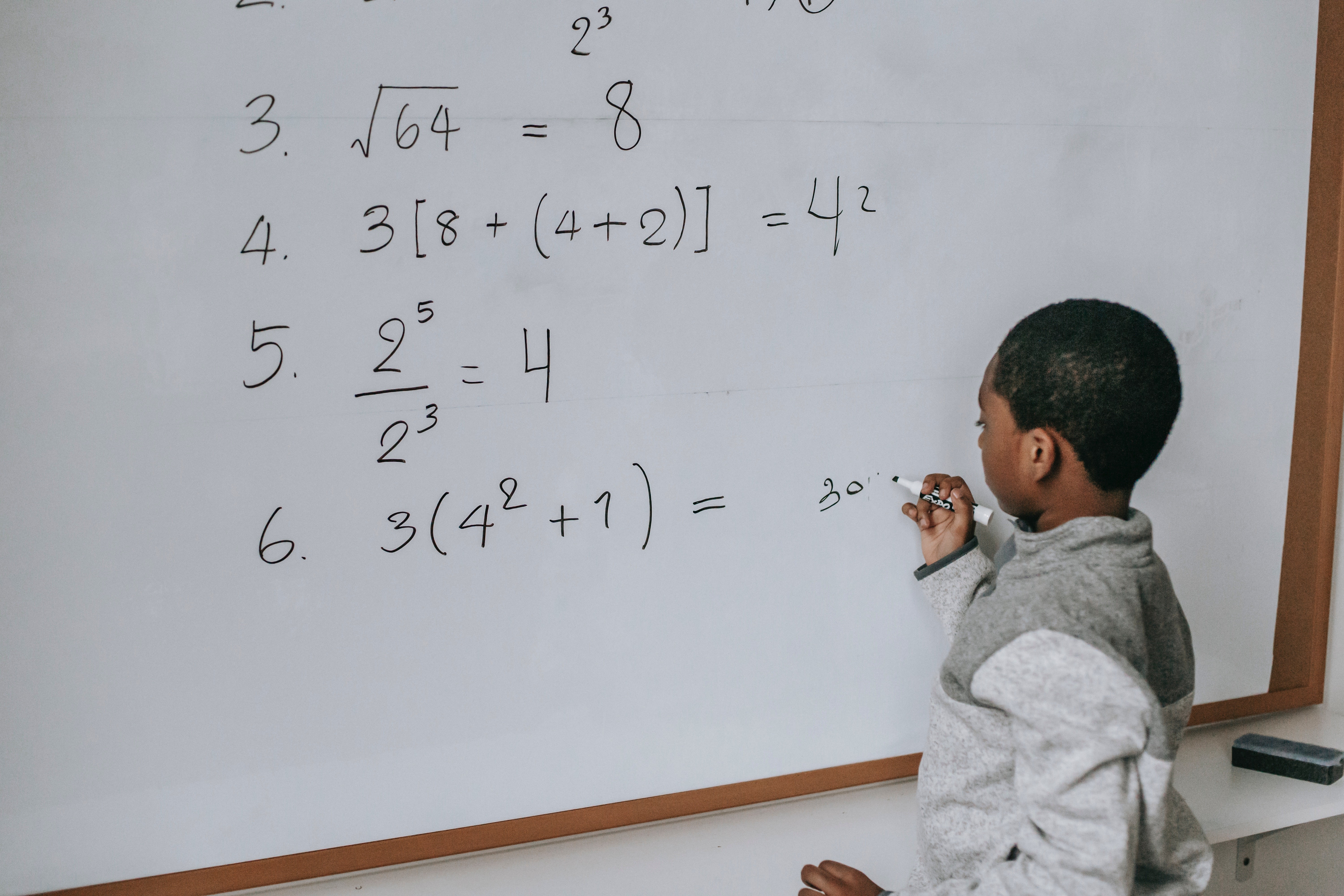 Young black student solving math equations on a dry erase board.