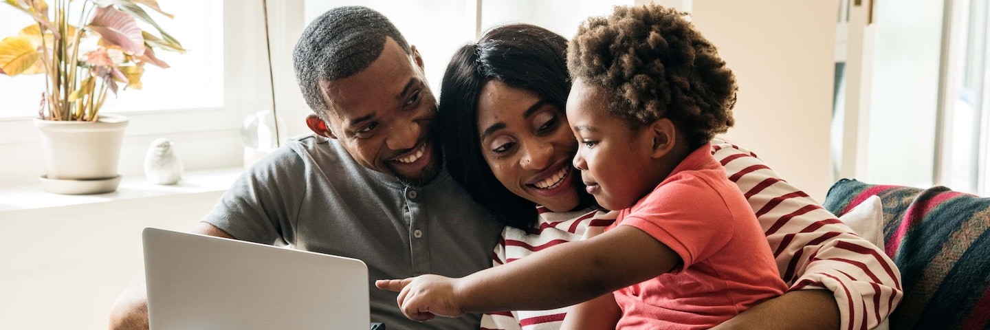 Two parents and a child smiling and using a laptop together.