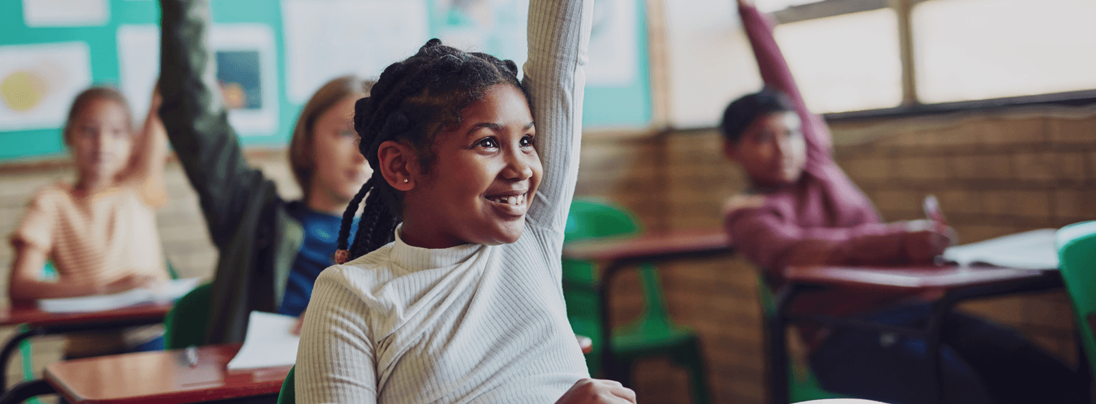 Eager students in a classroom with their hands up.