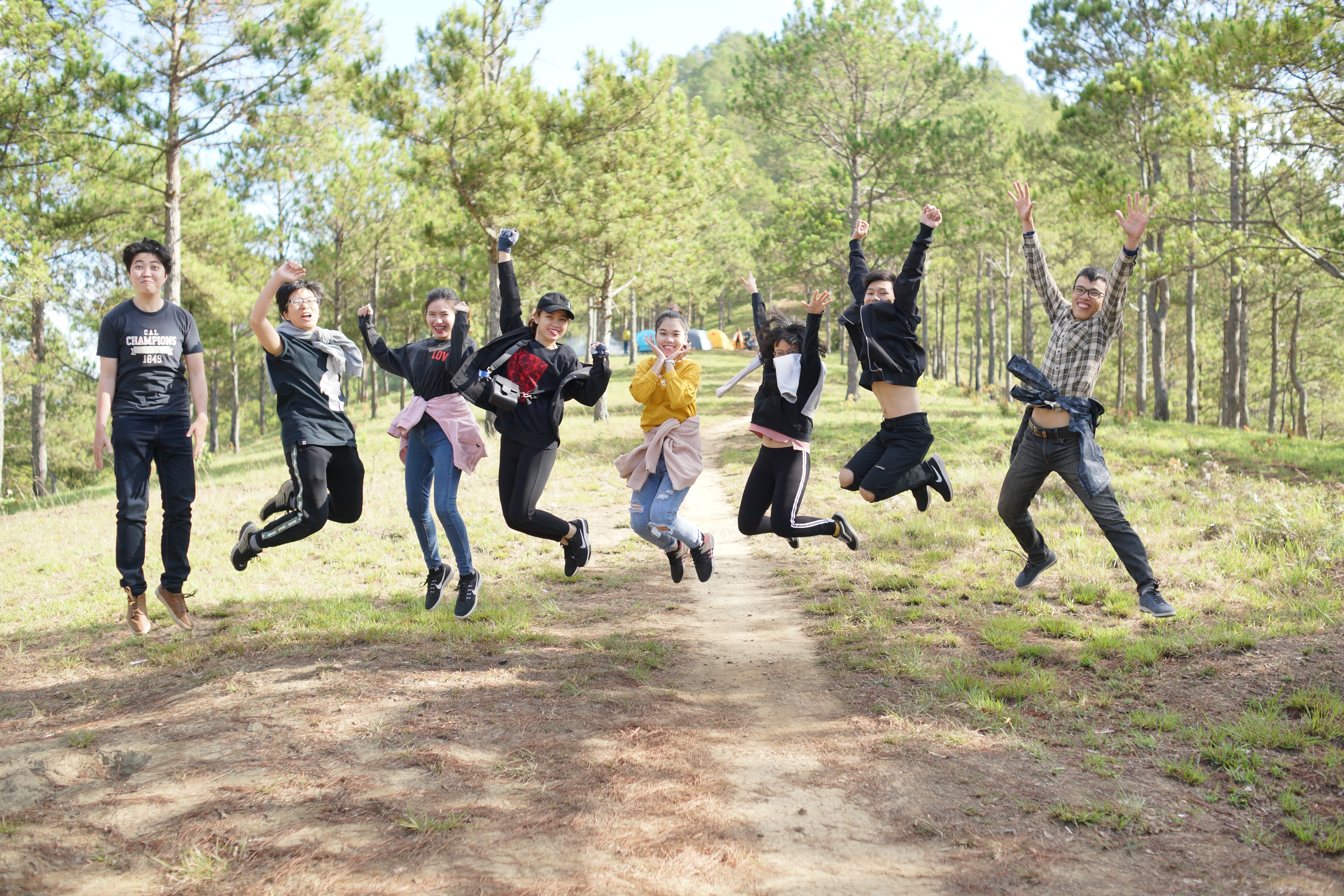 Eight students who are part of a classroom community jumping in unison with a forest in the background.