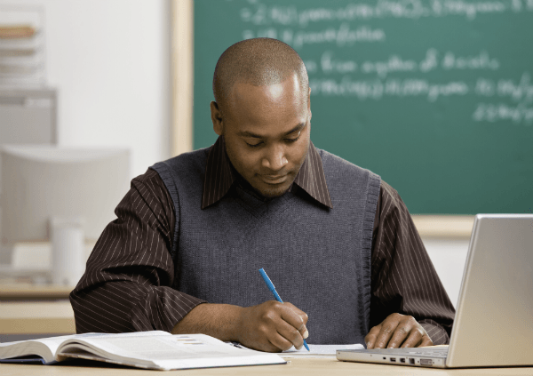 A teacher sits down at his desk, grading student work.
