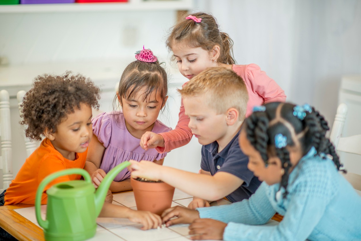 A group of five elementary students planting seeds in a clay flower pot.