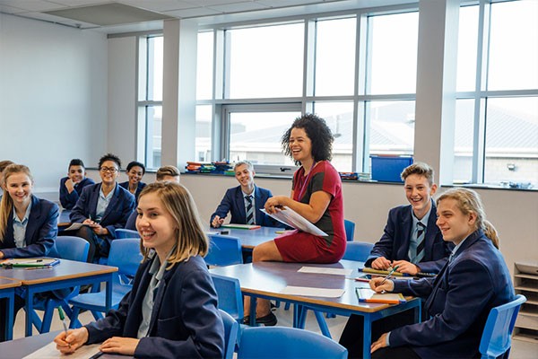 A teacher and high school students in school uniforms sit in a classroom.